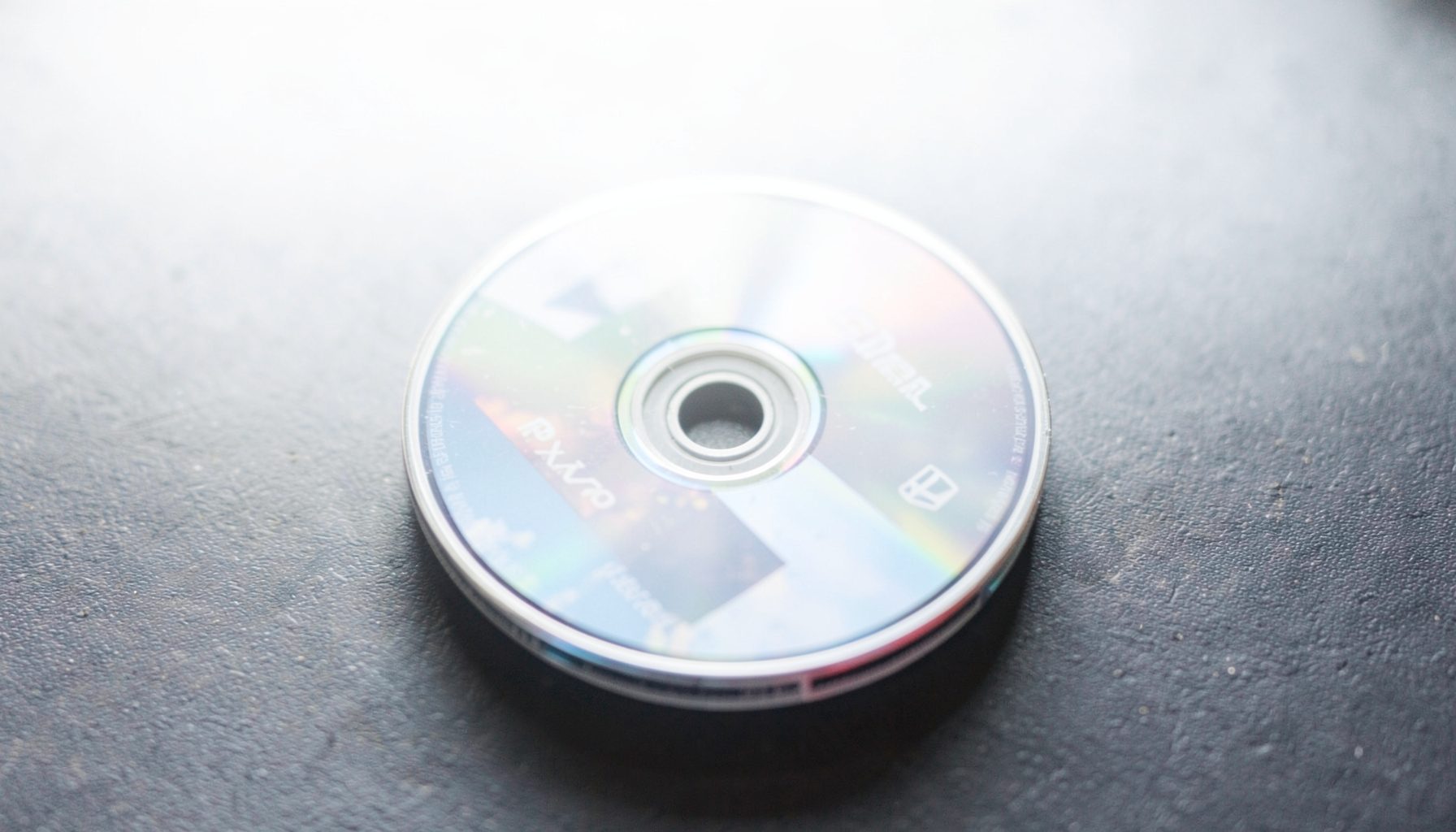 A bright, airy photograph of a classic PlayStation game disc with a reflective surface, resting on a dark textured background with soft side lighting.