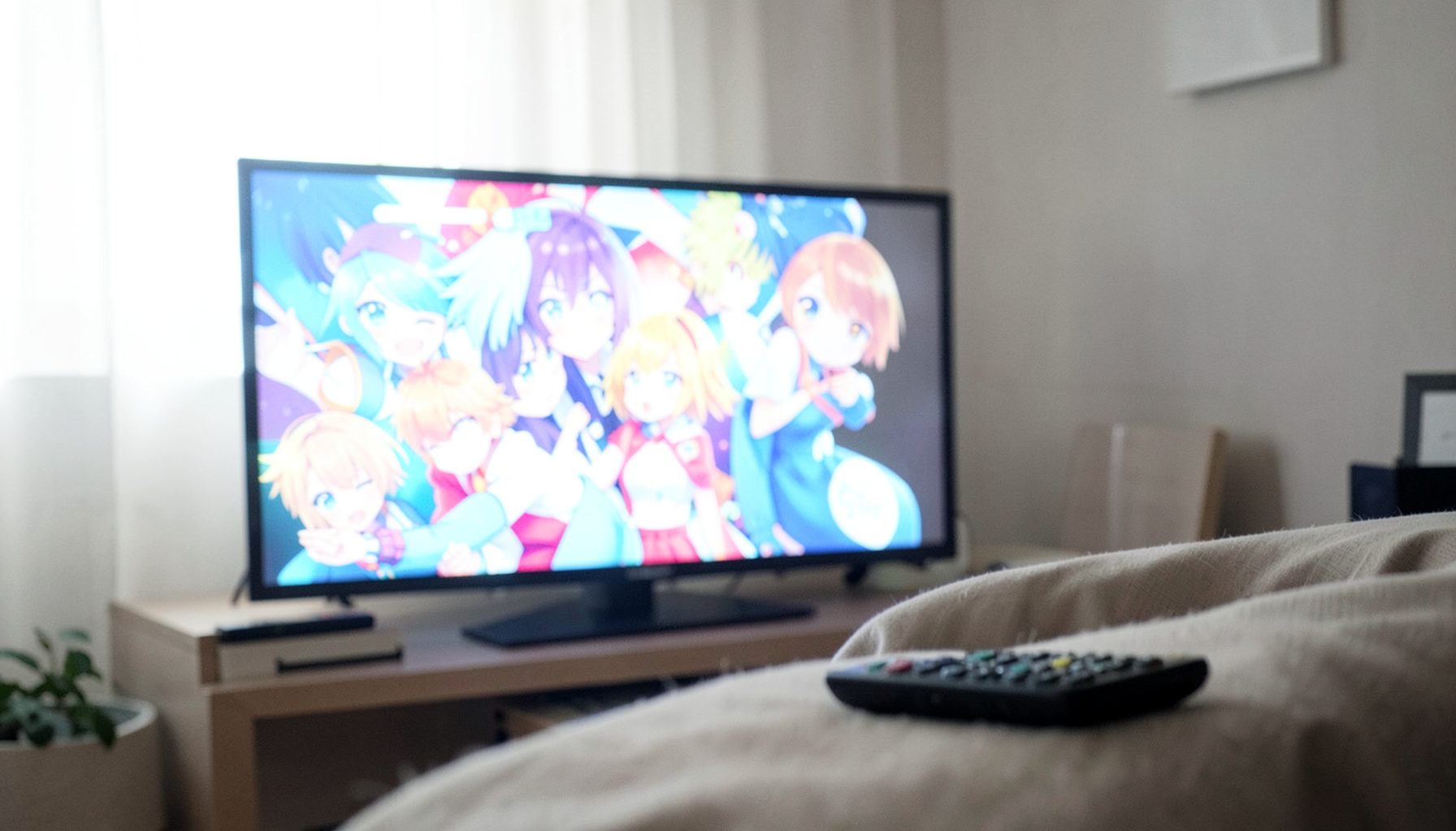A bright, airy photograph of a television screen glowing with vibrant anime visuals in a dimly lit living room, with a remote control resting on a cushion in the foreground.