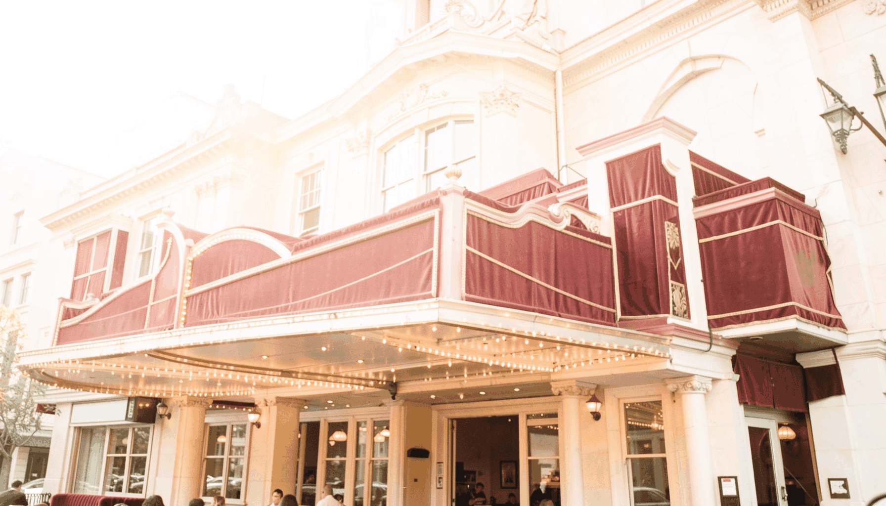 A bright, high-key photograph of a grand cinema facade with soft golden lighting and deep red velvet tones, suggesting a premiere event.